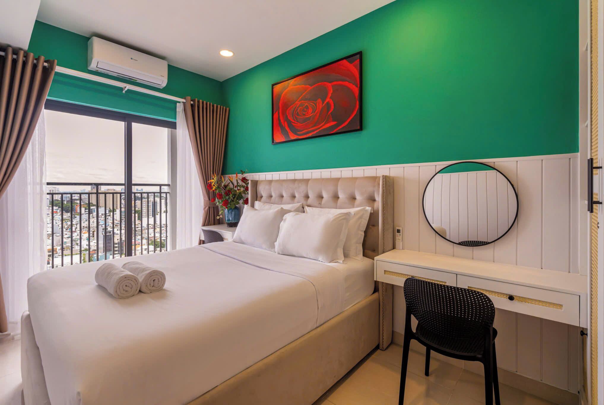 A hotel room with a bed, a desk, a chair, a round mirror, and a large window with curtains.