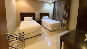 A hotel room with two beds, a wooden desk, and a large window with curtains. - Wow Grand Serviced Apartments (Jeddah)