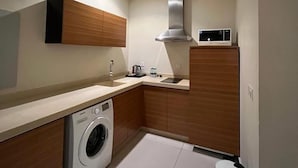 A compact kitchen with a washing machine, a microwave, and a stainless steel range hood. - Wow Grand Serviced Apartments (Jeddah)