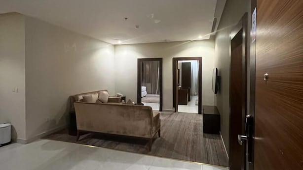 A spacious room with a large bed, a sofa, and a wooden door. - Wow Grand Serviced Apartments (Jeddah)
