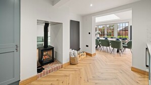 Een moderne woonkamer met een houtkachel, een eethoek met een tafel en stoelen, en uitzicht op de omgeving.