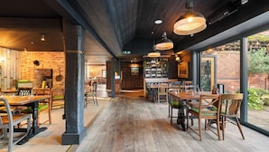 Een restaurant met houten vloeren, bakstenen muren en hangende吊りlichten. Tafels en stoelen staan klaar voor het diner.