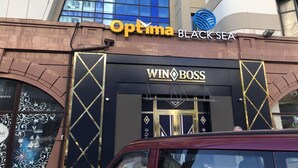 Um edifício com uma placa que indica 'Optima Blacksea' e 'Win Boss' no andar térreo.