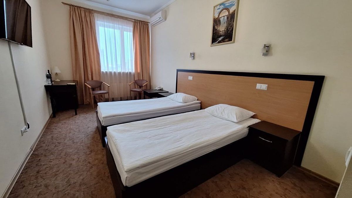 A hotel room with two single beds, a desk with a chair, a TV, and a painting on the wall.