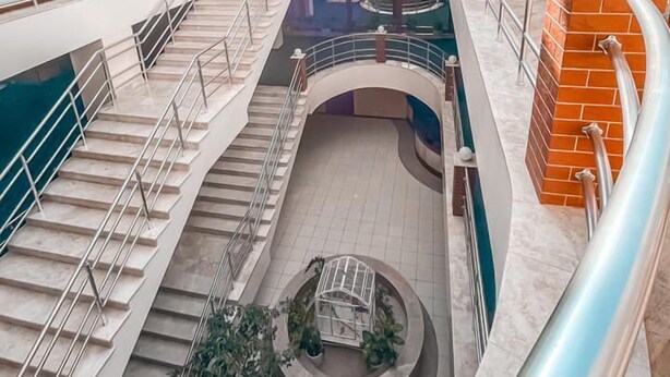 Um átrio de vários níveis com escadaria central, teto de vidro e área de estar circular.