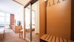 Quarto de hotel com cama, escrivaninha, cadeira, televisão e porta de vidro deslizante para uma varanda.