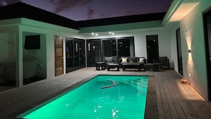 Een modern zwembad met terras, een lounge met banken en een salontafel, en een glazen patio.