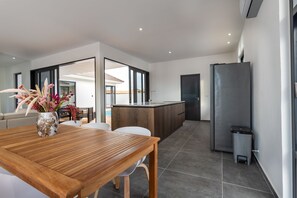 A modern kitchen with a central island, a dining area with a wooden table, and a built-in bench. - Brand New Immaculate 3-bed Villa in Grote Berg (Grote Berg)