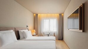 Una habitación de hotel con dos camas, una mesita, una silla y un televisor montado en la pared.