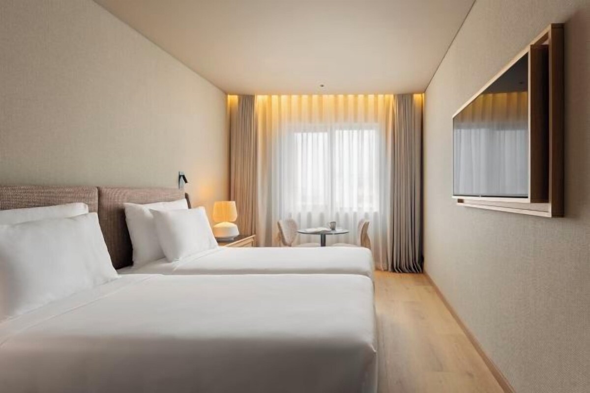 Een hotelkamer met twee bedden, een tafeltje, een stoel en een aan de muur bevestigde televisie.
