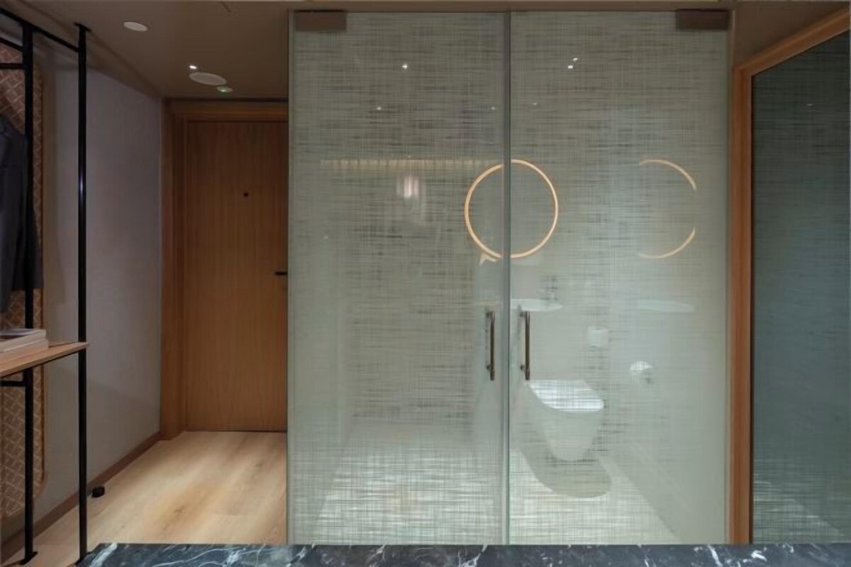Een moderne badkamer met een douche in een glazen cabine, een houten deur en een marmeren aanrechtblad.