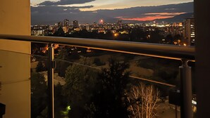 A balcony with a cityscape view at dusk, including buildings and a distant sunset. - MERDZ Spa & Fitness Sky Resident  (Skopje)