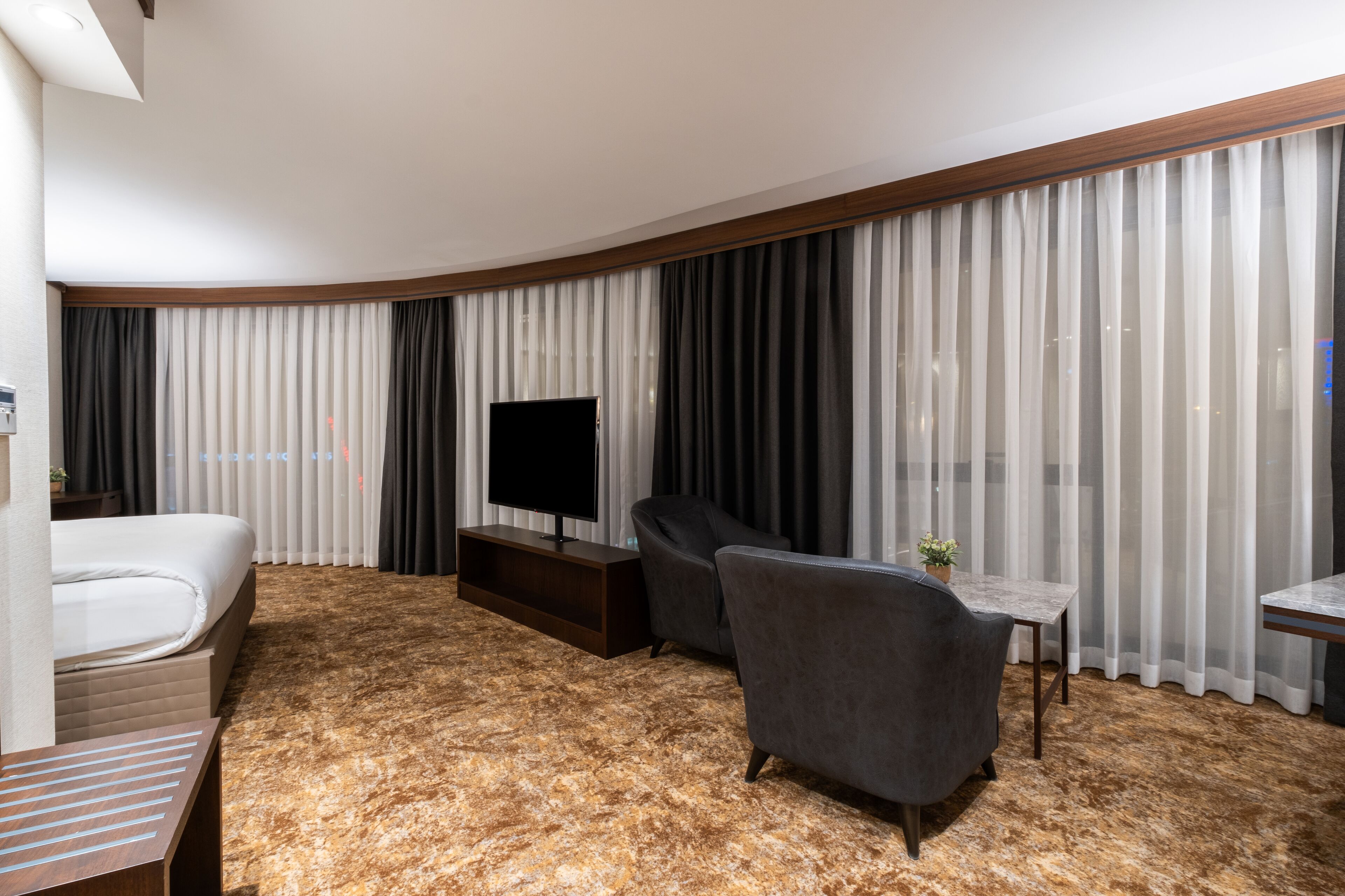 A hotel room with a bed, a TV, a sofa, a small table, and a carpeted floor.