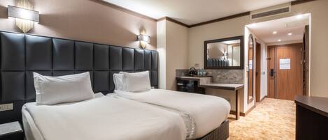 Habitación de hotel con una cama grande, una mesita de noche, un banco integrado, un tocador con espejo y una puerta que da a otra habitación.