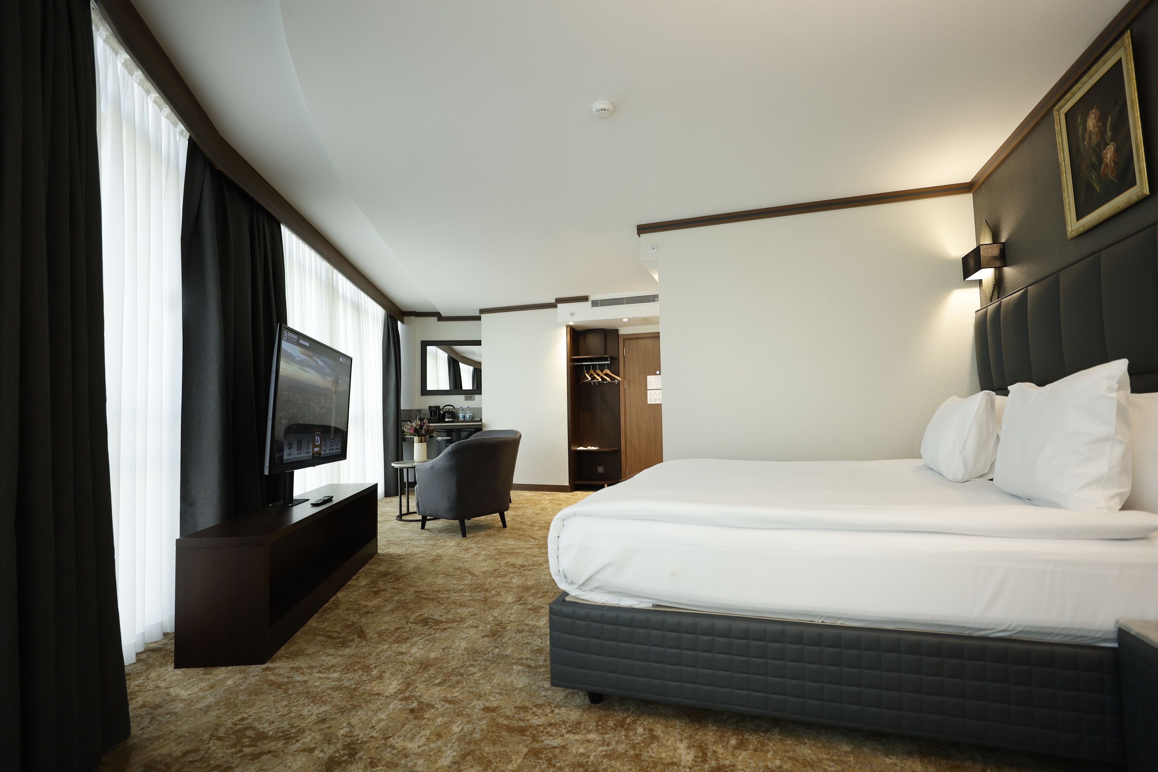 A hotel room with a large bed, a TV on a stand, a desk with a chair, and a wardrobe.