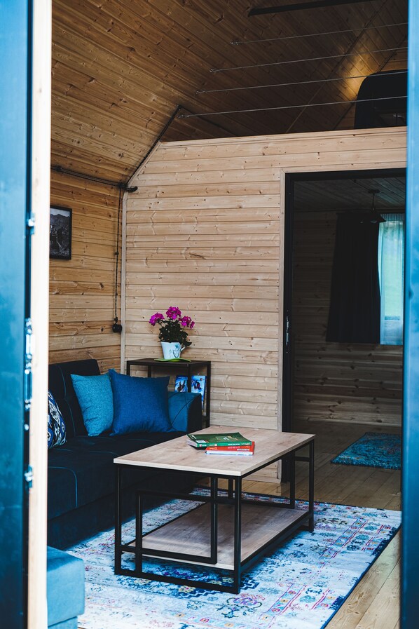 A cozy room with wooden walls, a blue sofa, a coffee table, and a patterned rug. - Traveler's Cottage in Kazbegi (Kazbegi)