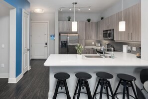 A modern kitchen with a large island, bar stools, stainless steel appliances, and pendant lighting. - Luxury Serviced Apartment in Uptown CLT (Charlotte)