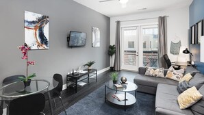 A modern living room with a glass dining table, a grey sofa, and a ceiling fan. - Luxury Serviced Apartment in Uptown CLT (Charlotte)