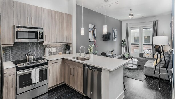 A modern kitchen with stainless steel appliances, a dishwasher, and a large island. There is a dining area with a sofa and a coffee table. - Luxury Serviced Apartment in Uptown CLT (Charlotte)