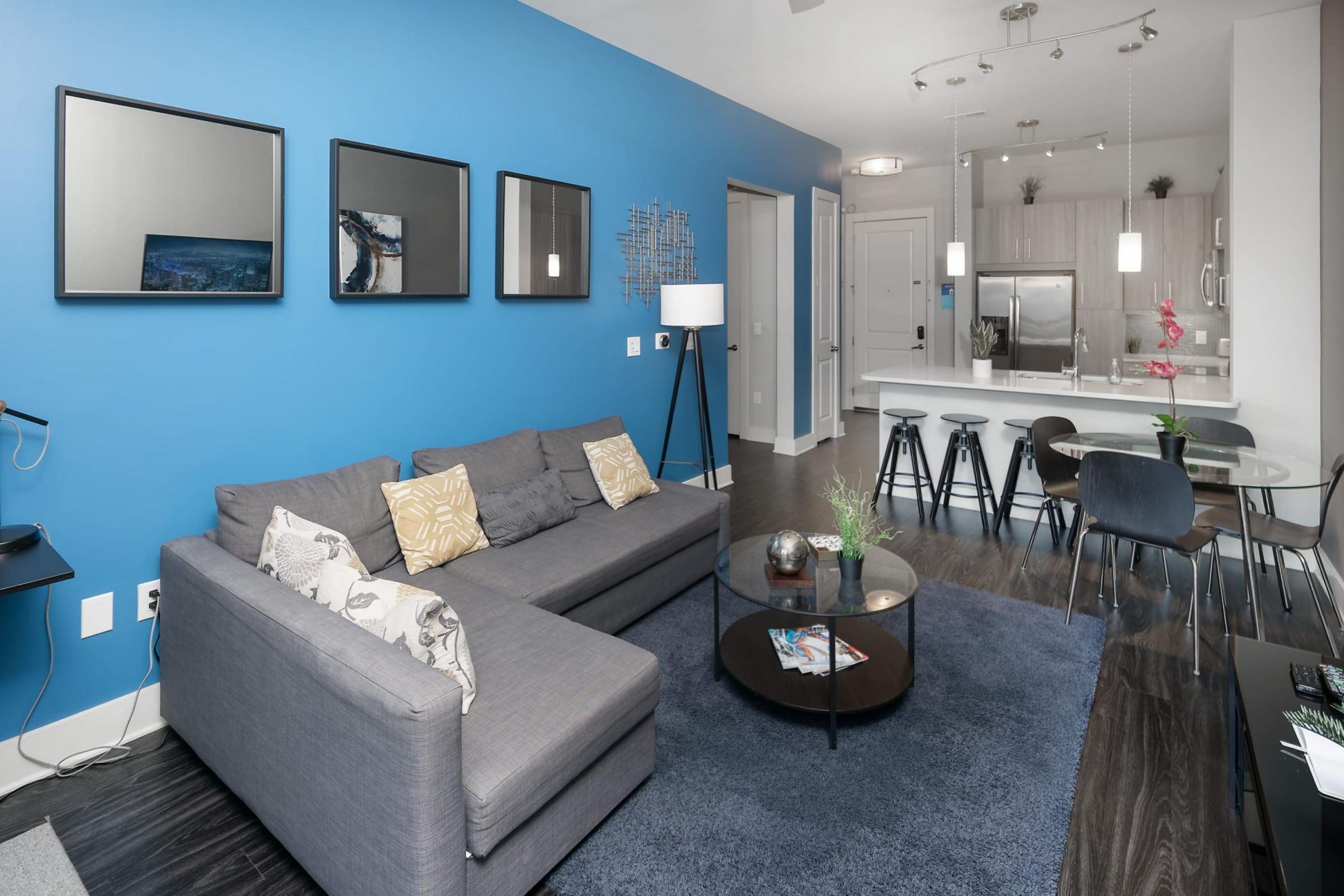 Un salon moderne avec un canapé d’angle gris, une table basse ronde et un mur d’accent bleu.