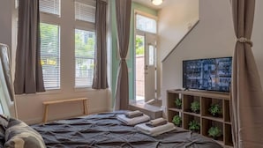 A bedroom with a bed, curtains, a TV, and a shelf with plants. - 2 Bedroom Hip Apartment, Free Parking & Wifi (Charlotte)