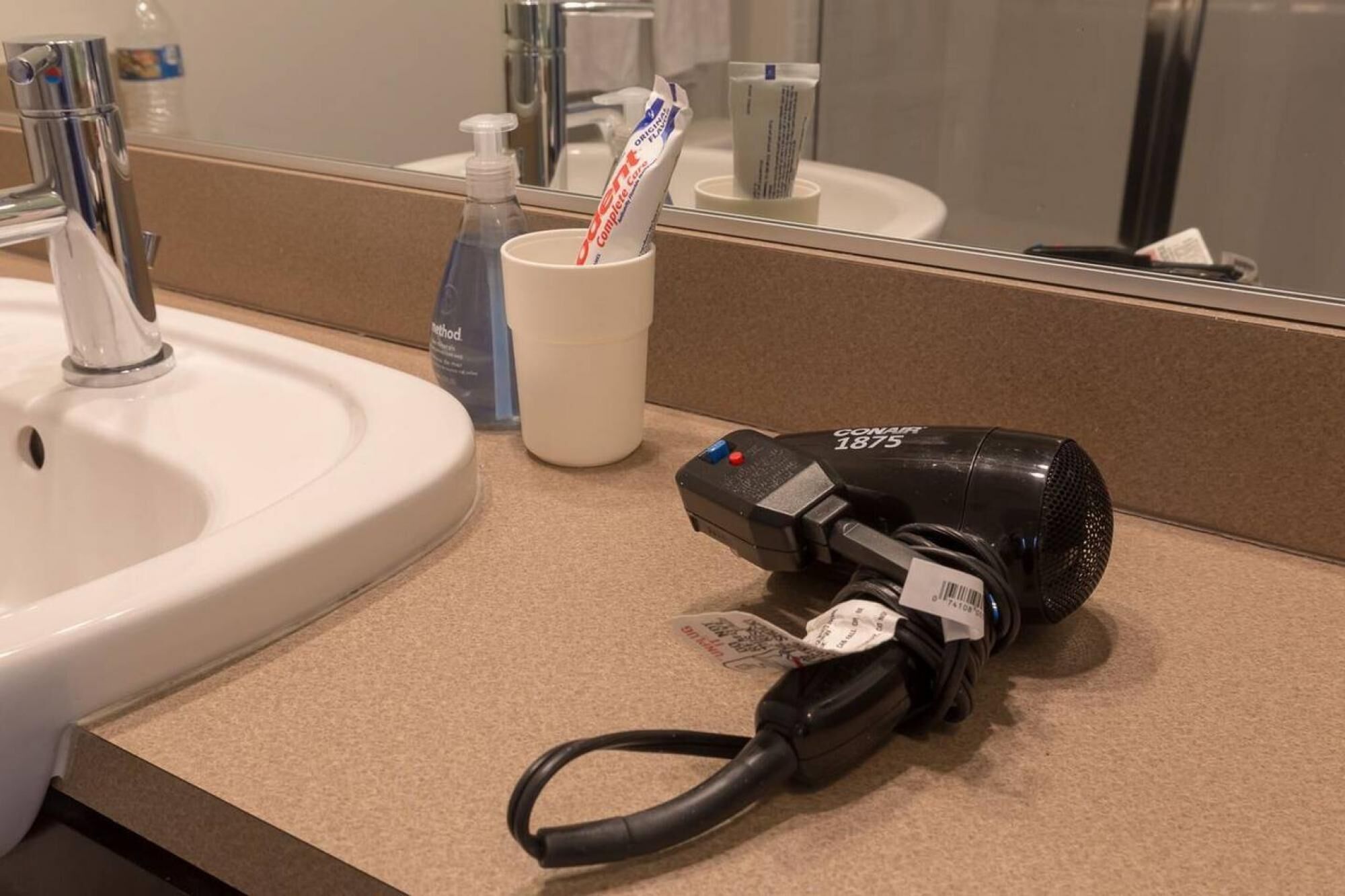A bathroom sink with a mirror, a white cup, and a hairdryer plugged in.