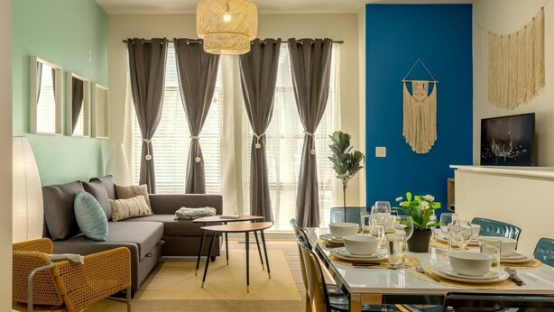 A living room with a sofa, dining table, and chairs. There is a window with curtains, a hanging light fixture, and a wall-mounted macrame decoration. - 2 Bedroom Hip Apartment, Free Parking & Wifi (Charlotte)