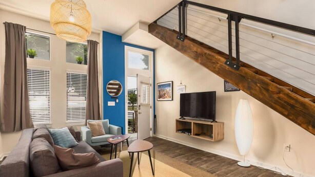 A modern living room with a sofa, a coffee table, and a TV. There is a staircase with a wooden railing and a blue door. - Apartment 10 Min Walk to Epicenter with Wifi (Charlotte)
