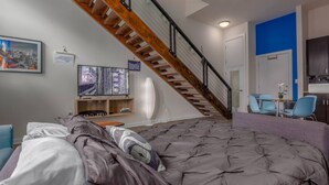 A bedroom with a large bed, a wooden staircase, a television, and a cityscape artwork on the wall. - Apartment 10 Min Walk to Epicenter with Wifi (Charlotte)
