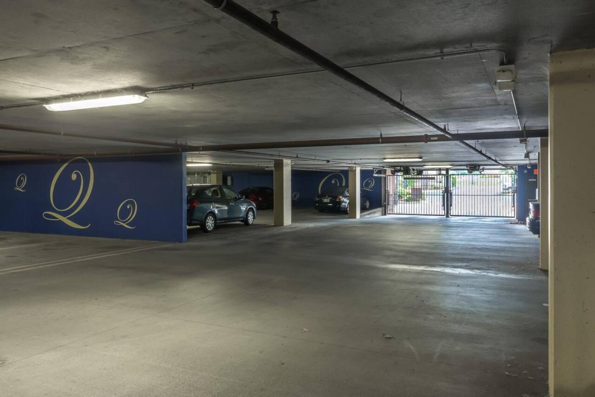 A multi-level parking garage with concrete floors and walls, featuring a blue mural with a large 'Q' on the left wall.