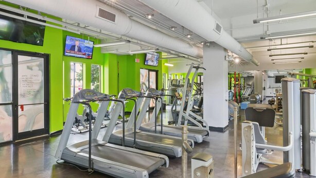 Une salle de sport équipée de tapis de course, d’appareils de musculation et d’un téléviseur fixé au mur.