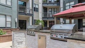 Un espace cuisine extérieur comprenant deux barbecues, une cheminée en pierre et un parasol rouge.