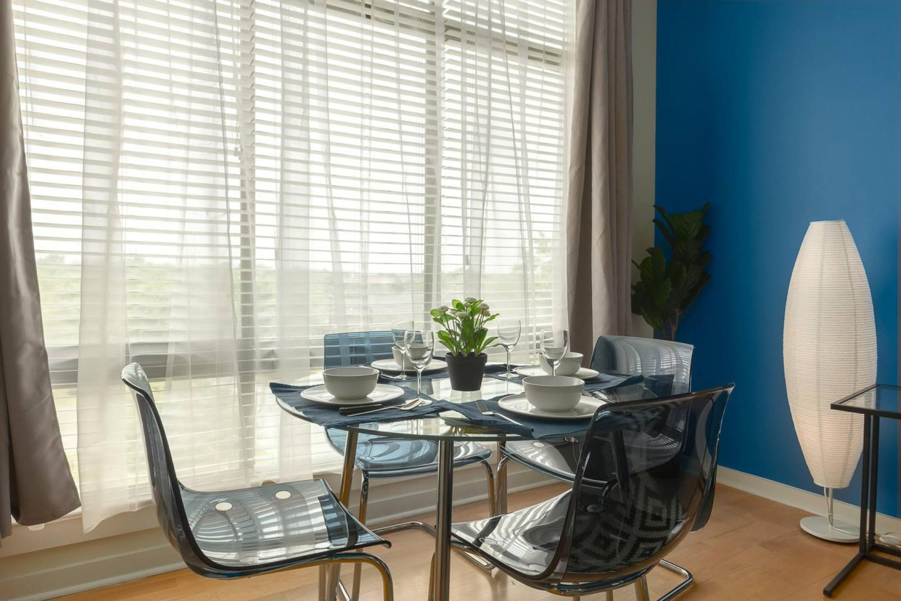 Uma sala de jantar com mesa de vidro posta para quatro pessoas, cercada por cadeiras modernas.