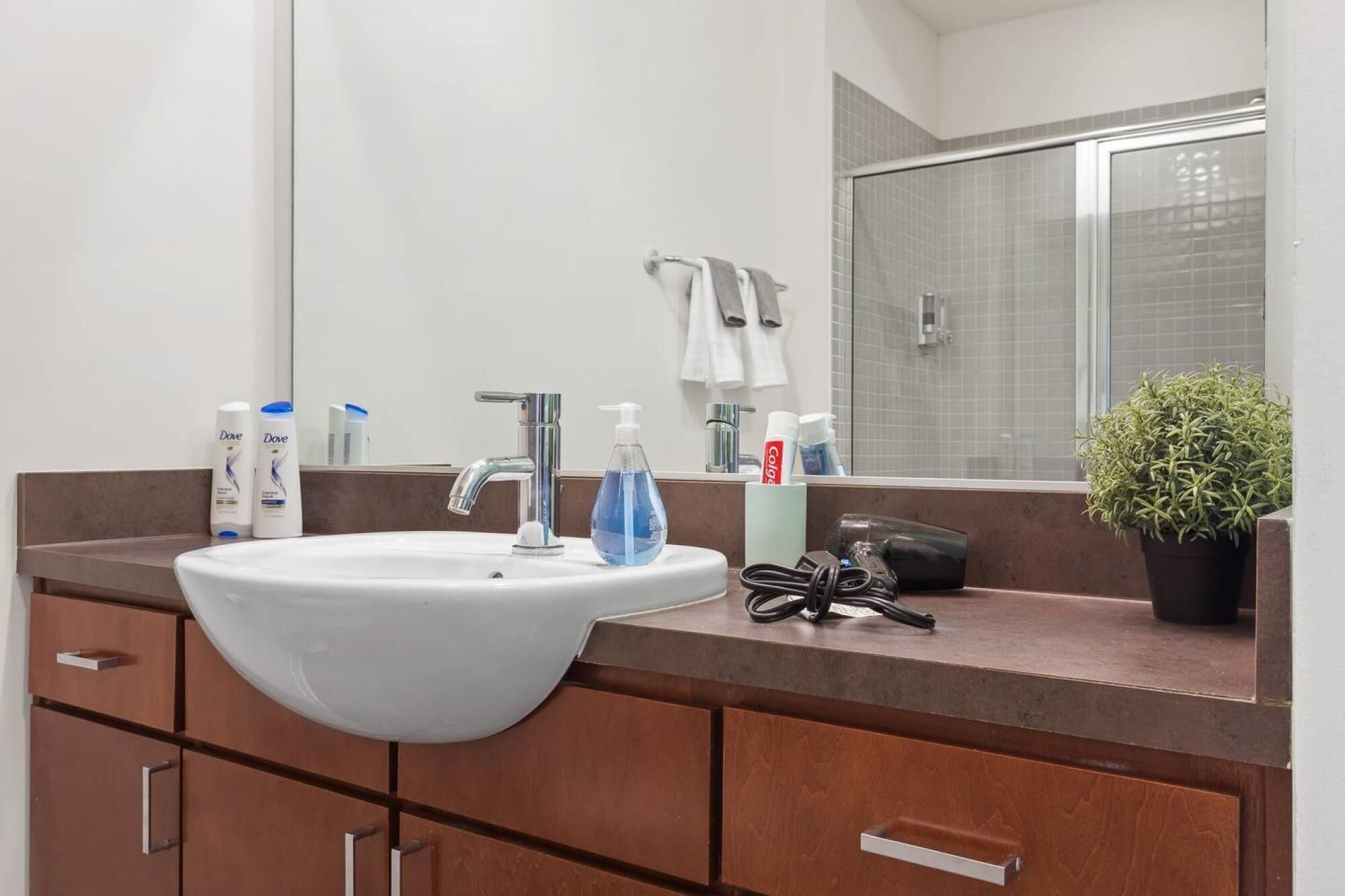 A bathroom with a white sink, a mirror, and a shower. There are toiletries on the counter, including Dove shampoo and body wash.