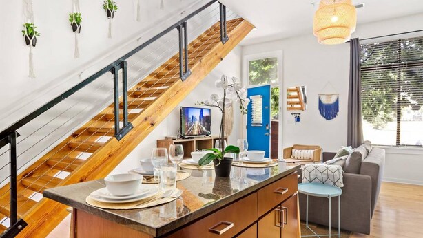 A modern kitchen with a wooden staircase, a dining area with a round table, and a living room with a sofa and a TV. - One Bedroom Apartment -10 Min Walk to Epicentre Wifi (Charlotte)