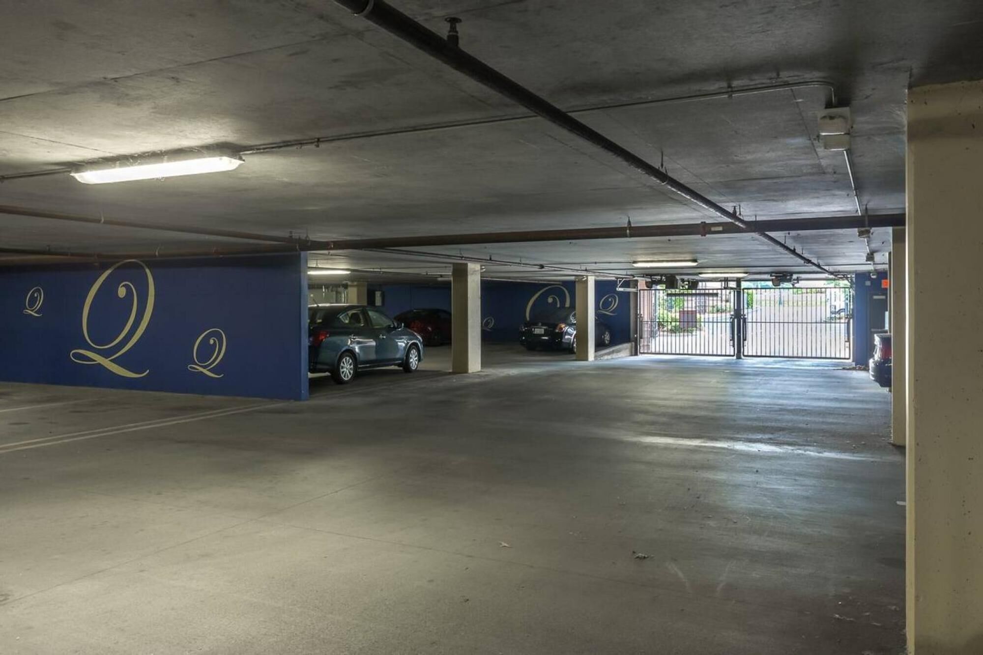 A multi-level parking garage with concrete floors and walls, featuring a blue wall with a large 'Q' symbol.