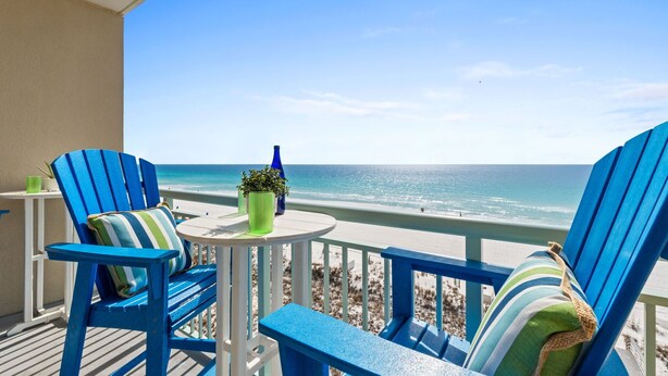 A balcony with two blue Adirondack chairs, a small round table, and a potted plant. - PI 613: Salty Sunsets - Beachfront Bliss with Unmatched Ocean Views (Fort Walton Beach)