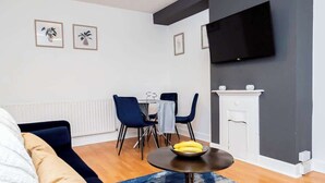 Ein modernes Wohnzimmer mit einer Couch, einem Esstisch mit Stühlen, einem an der Wand montierten Flachbildfernseher und einem Kamin.