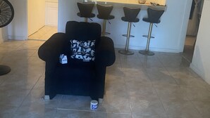 Una habitación con un sillón negro, un ventilador y tres taburetes.