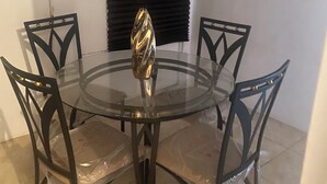 Una mesa redonda de vidrio con cuatro sillas, cada una con estructura metálica y asiento de plástico.