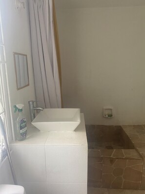 Une salle de bain avec un lavabo blanc, une douche et un espace de douche carrelé en pierre.