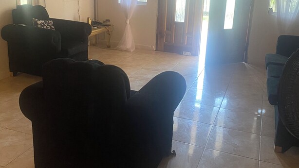 Una habitación con techo de madera, sofá negro, televisor montado en la pared y una puerta con ventanal.