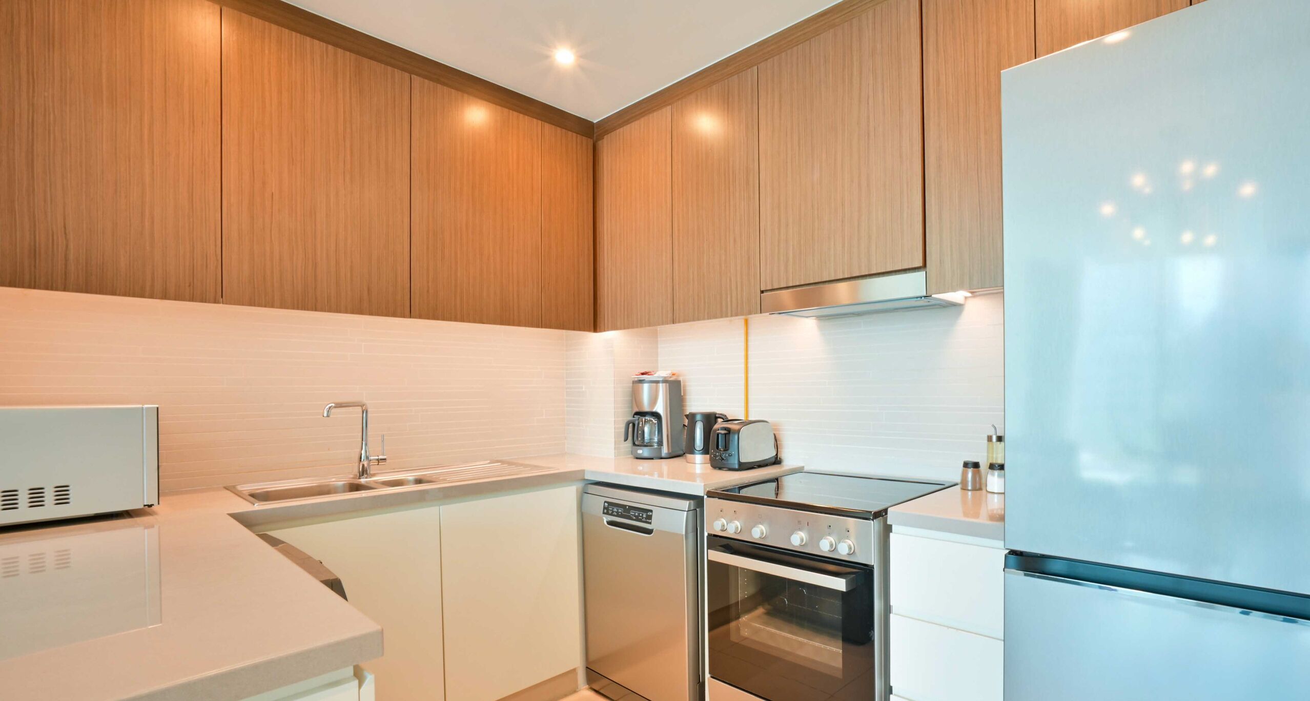 A modern kitchen with wooden cabinets, a stainless steel dishwasher, a built-in oven, a refrigerator, and a coffee maker.