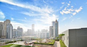A modern urban residential area with high-rise buildings, a well-maintained courtyard with greenery, and a clear sky.
