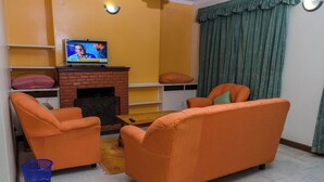 A living room with two orange sofas, a brick fireplace, and a television on a shelf.