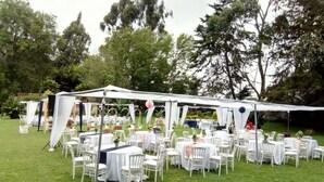 An outdoor event space with round tables and white chairs, covered by a white tent.