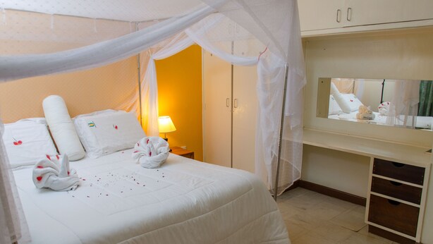 A neatly made bed with a canopy, a bedside lamp, and a mirror above a dresser.