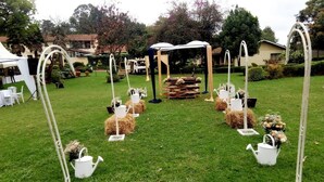 A grassy outdoor area with a white tent, hay bales, and white watering cans arranged in a circle.