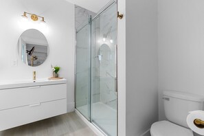 A modern bathroom with a glass-enclosed shower, a white vanity with a mirror, and a toilet.