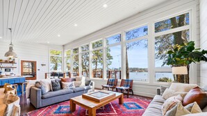 A spacious living room with a large window overlooking a body of water, a cozy seating area, and a wooden coffee table. - Lakefront Escape | Private Dock | Sleeps 24 (Hot Springs)